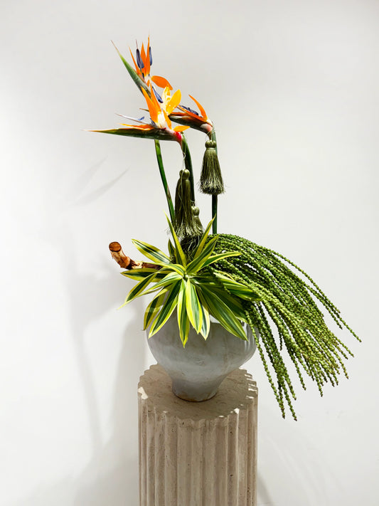 Flower delivery in Dubai: A modern arrangement with bird of paradise flowers, green dracaena leaves, cascading pea-like stems in a gray ceramic vase